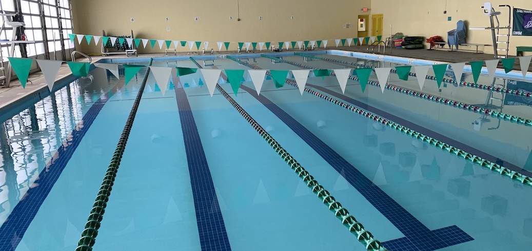 An indoor swimming pool with clear blue water, lane lines, and green and white penn