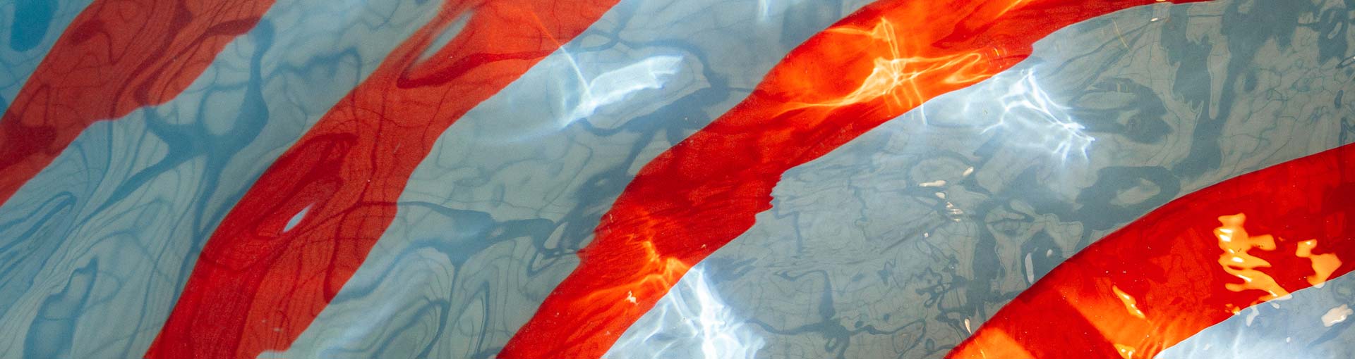 Diagonal red and blue stripes are distorted by shimmering water ripples with sun reflections.