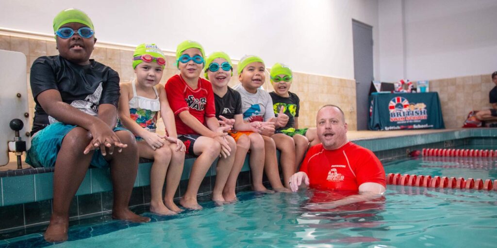Little kids sitting along edge of pool learning from swim instructor in pool
