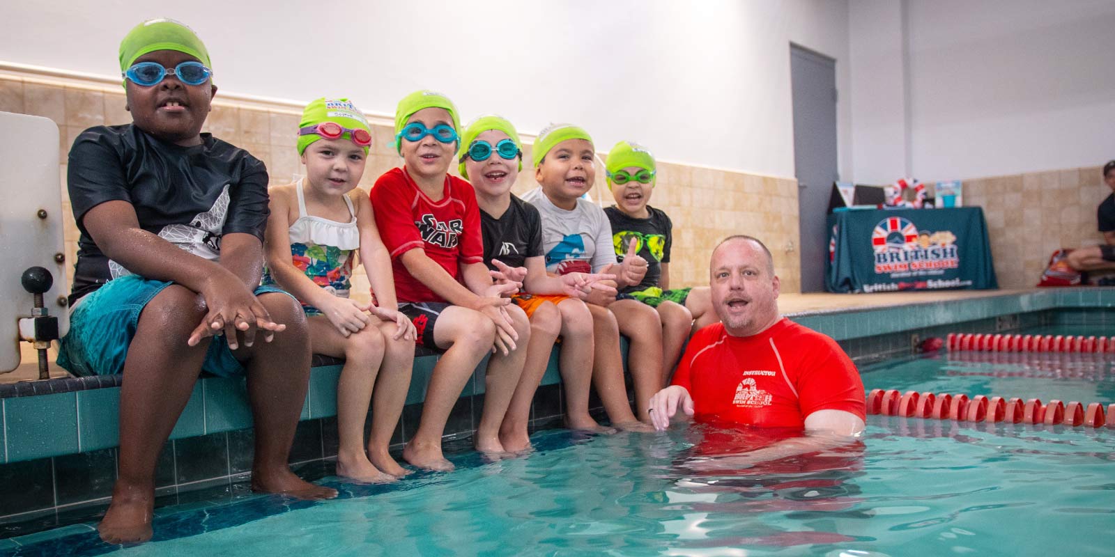 Little kids sitting along edge of pool learning from swim instructor in pool