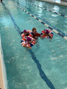 Shelby in the pool with three young students in inner tubes