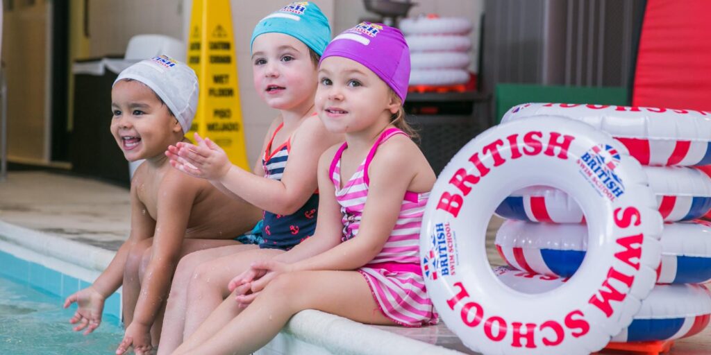 Children sitting on edge of pool smiling during their swim lesson
