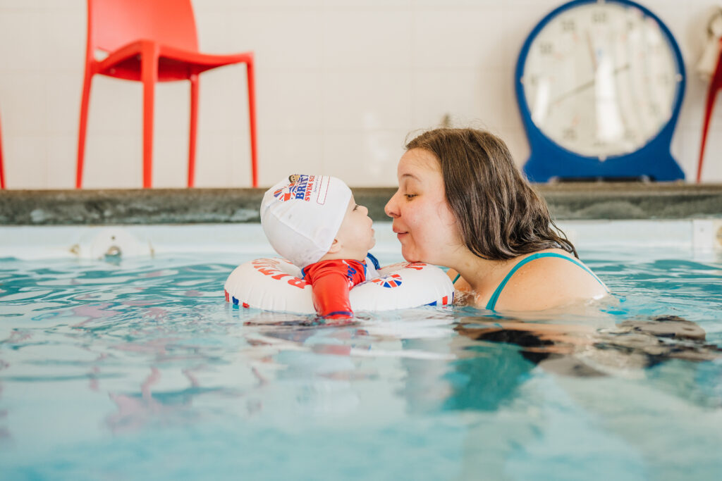 A parent and baby in British Swim School swim cap and floating ring share a quiet moment together during an infant swim lesson at British Swim School of Austin.