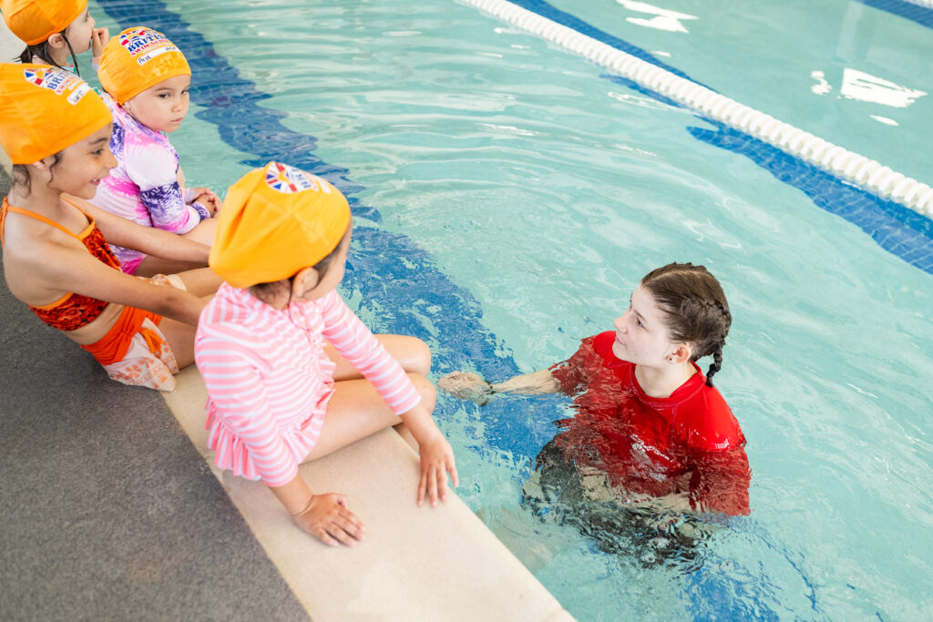 Small group lesson at British Swim School of Austin with the instructor and young swimmers sitting on the pool's edge.