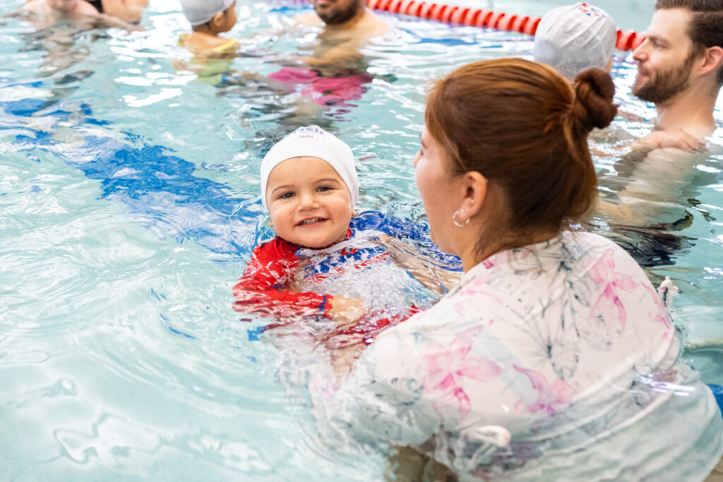 Young toddler learning to float with their guardian in an indoor heated pool at British Swim School.