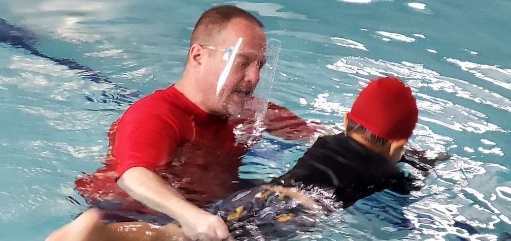 Swim instructor teaching a swimming lesson while wearing a face shield