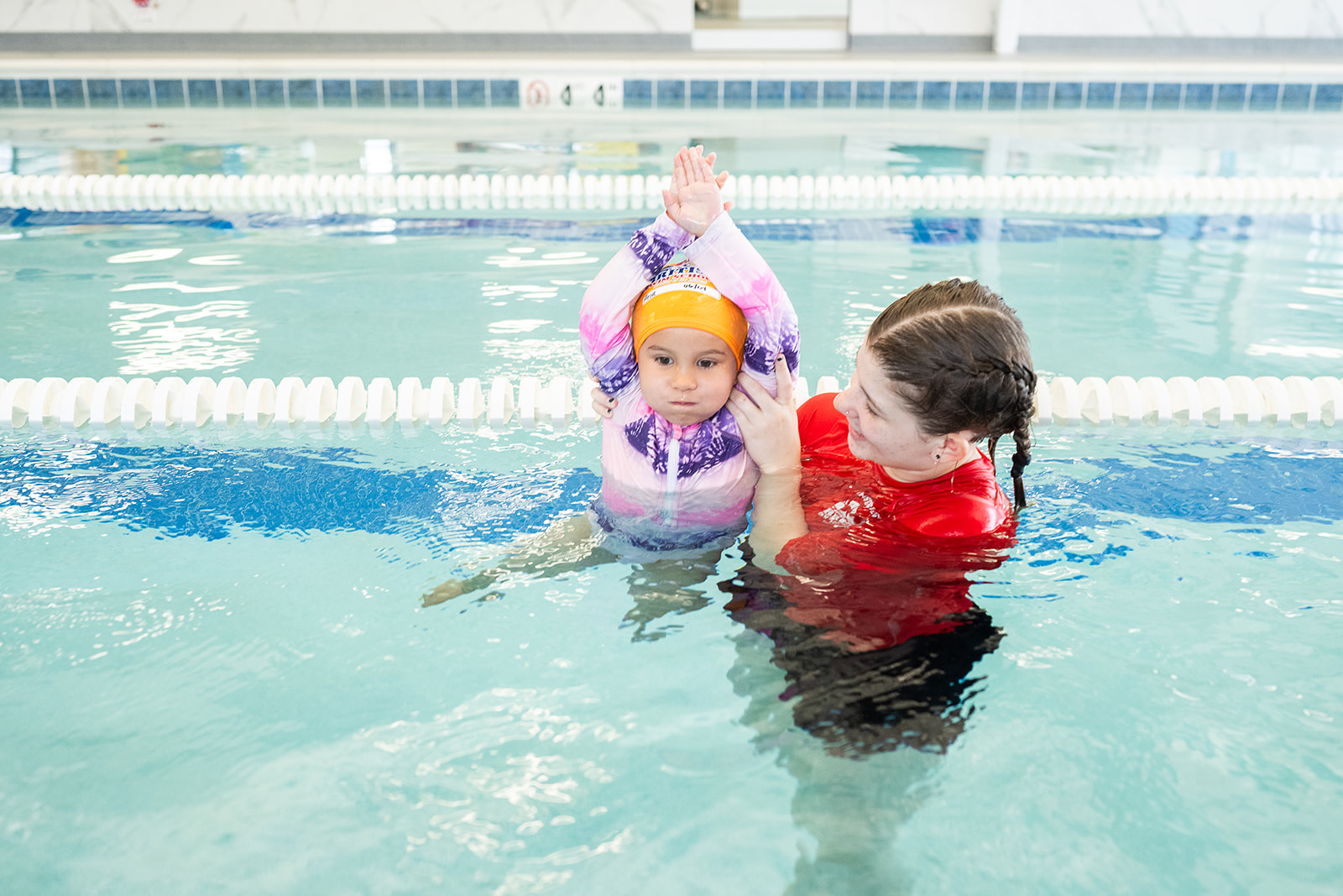 A swim instructor helps a young child practice in a bright indoor swimming pool. TITLE