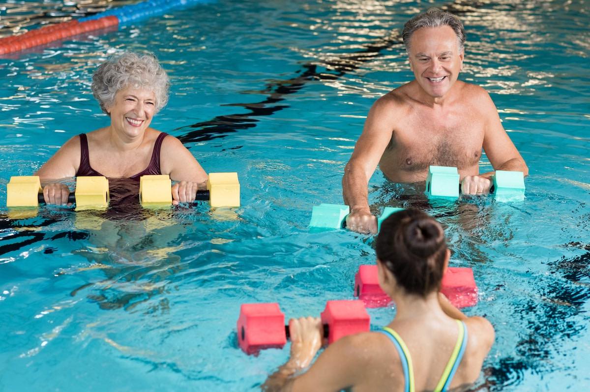 Two smiling seniors and a younger woman exercise with water weights in a pool.
