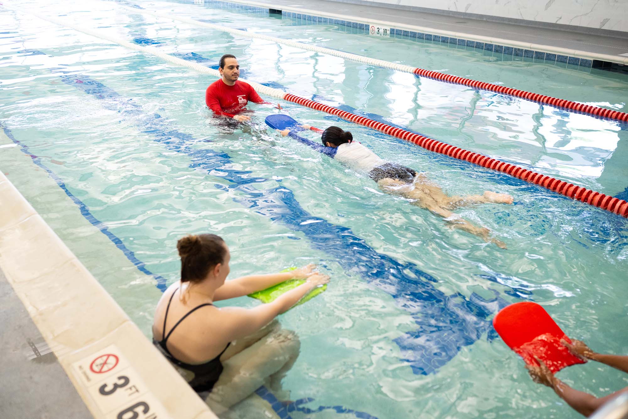 A swim instructor teaches two students in a clear indoor swimming pool.