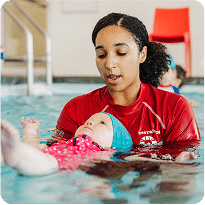 A swim instructor gently supports a baby floating on its back during a swimming lesson.