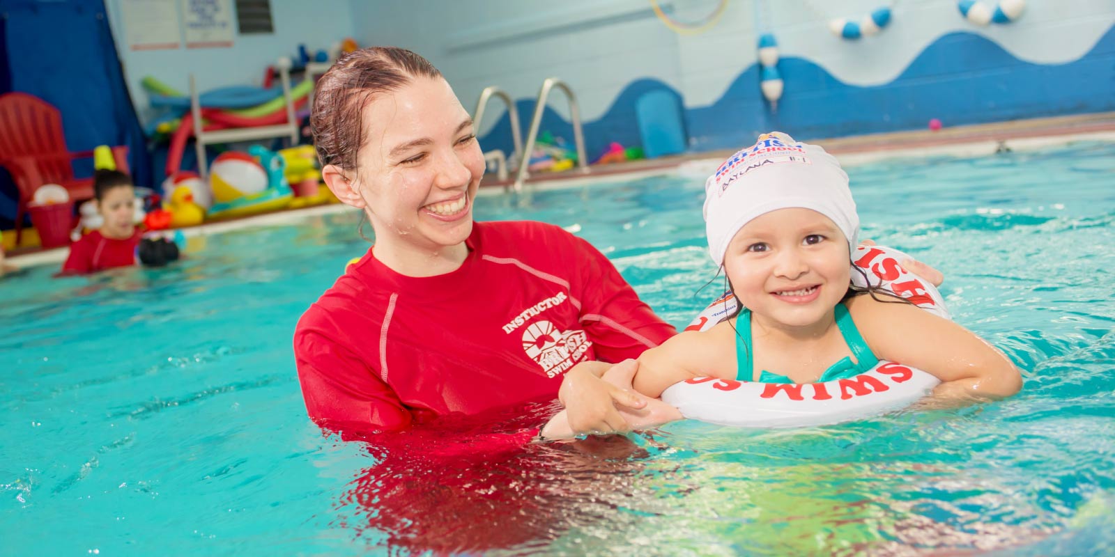 Niña pequeña sonriendo mientras recibe clases de natación de un instructor de British Swim School