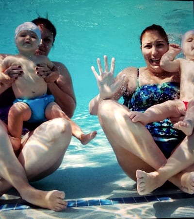 Dos mujeres sosteniendo bebés en sus regazos bajo el agua en una piscina