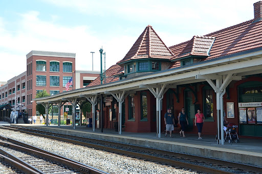 A charming red-brick train station with a tiled roof and covered platform next to