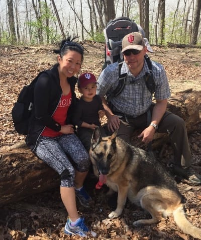 Katie and Greg seated on a log with their child and dog