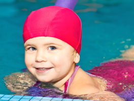 Little girl in pink swim cap smiling about to start swim lessons