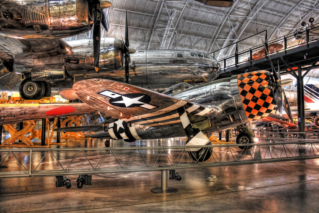 A polished silver fighter plane with a checkered nose and striped wings is displayed in a museum