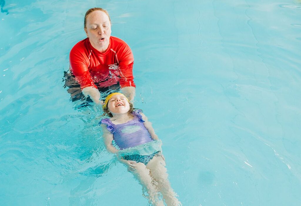 Young girl practicing a back float with support from a swim instructor during a British Swim School lesson in North Colorado Springs.
