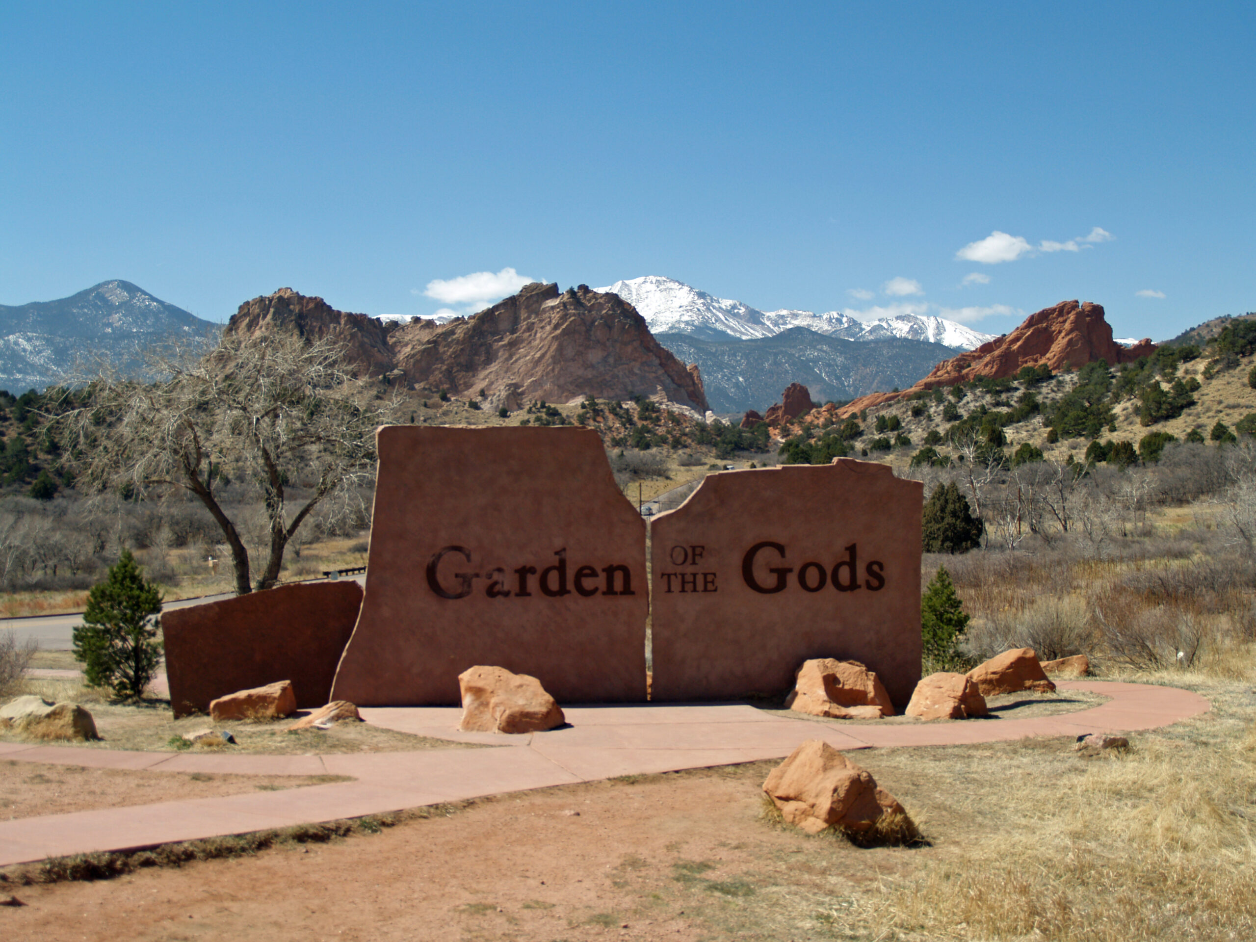 The iconic split rock entrance sign for the Garden of the Gods Park in Colorado Springs, featuring majestic snow-capped Pikes Peak and dramatic red rock formations under a clear blue sky. British Swim School offers year-round, indoor swim lessons for the El Paso County community and surrounding Colorado Springs, Manitou Springs, Fountain, and Monument neighborhoods.