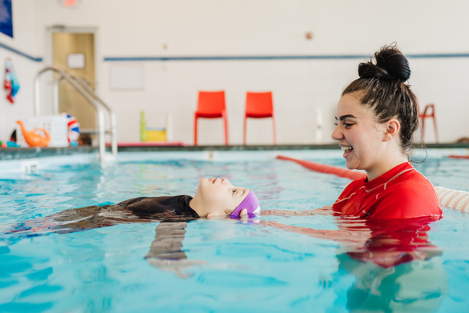 British Swim School instructor assists a smiling child with a back float lesson at the Darien-Lemont pool.