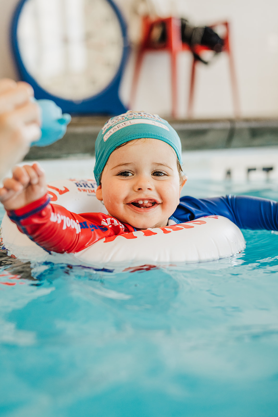 A joyful baby in a swim cap and float smiles brightly in a blue swimming pool.