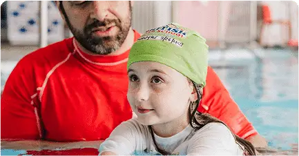 An instructor helps a young girl in a green swim cap during a swimming lesson. TITLE