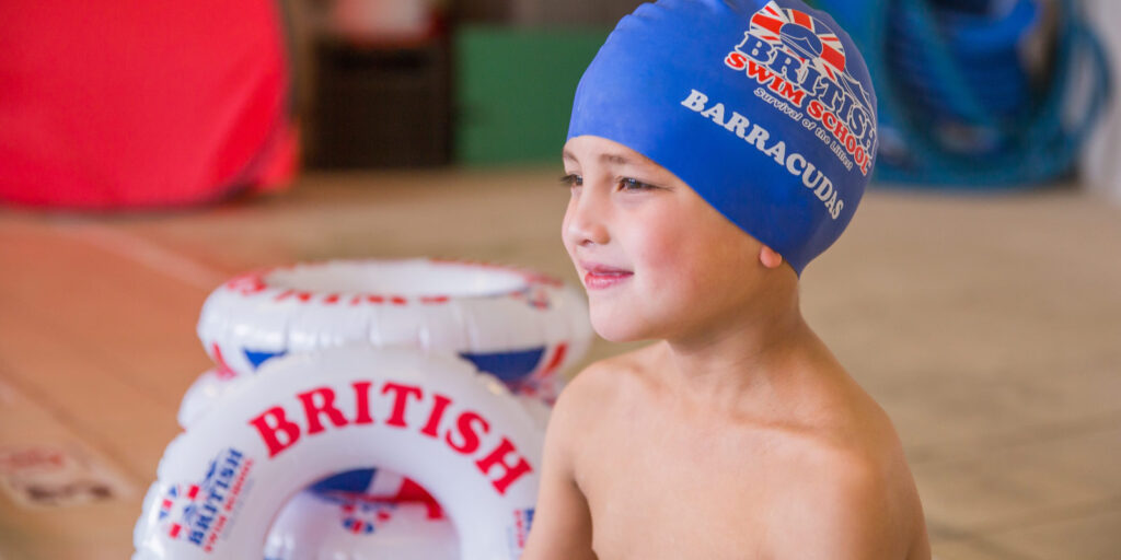Child in a British Swim School Barracuda class swim cap smiling