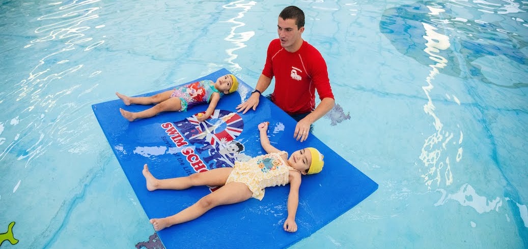 British Swim School Instructor teaching two young children how to swim