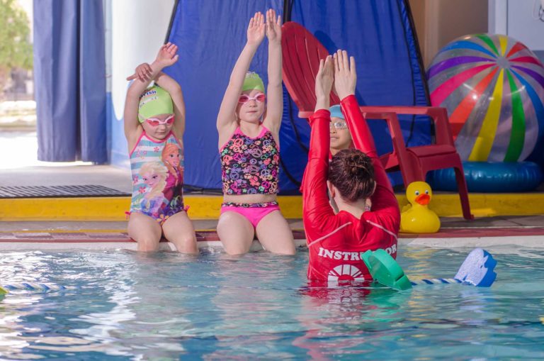 Children at swim lessons putting arms in the air like instructor