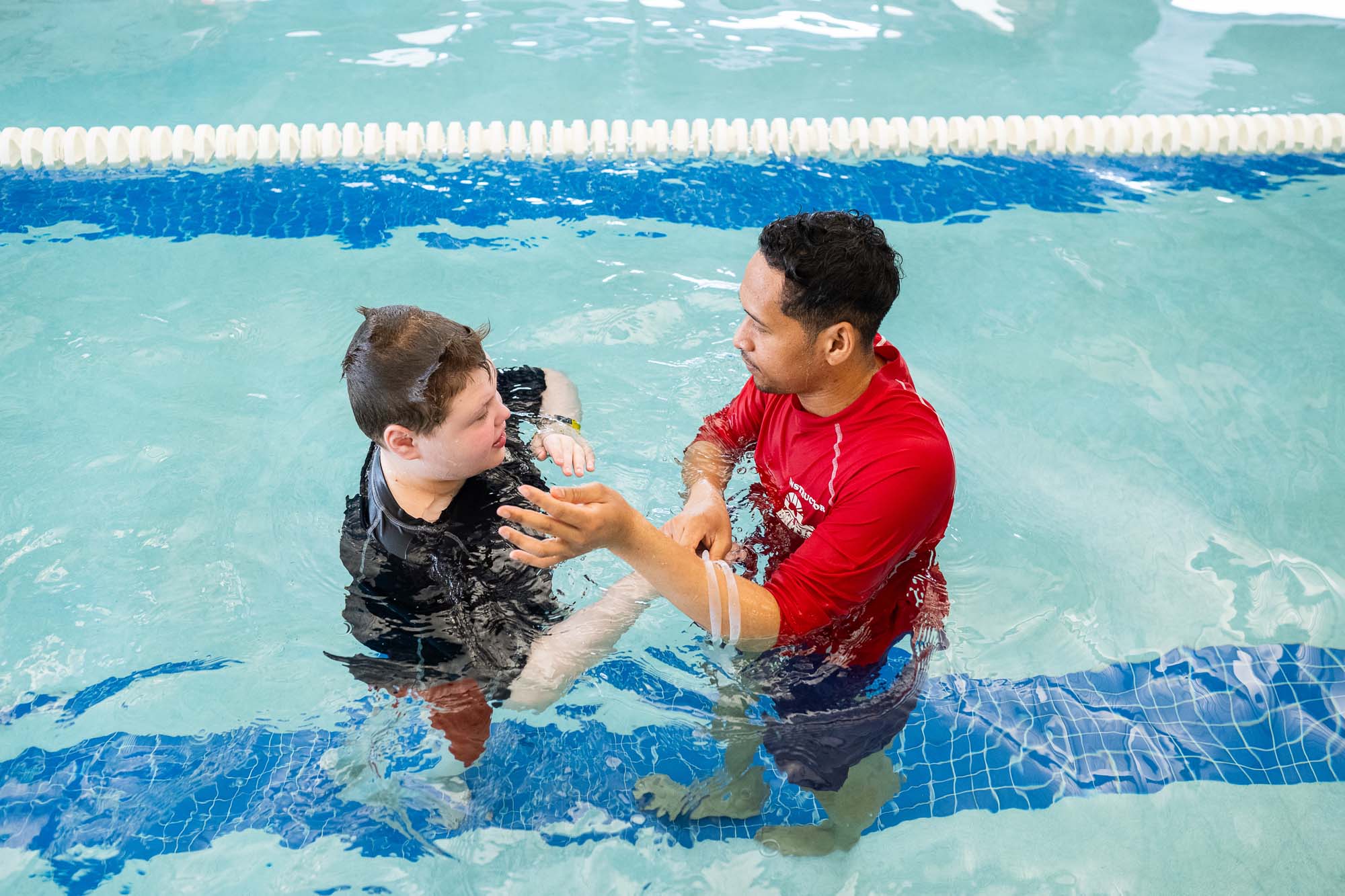 A swim instructor gently guides a young person with Down syndrome during a swimming lesson in a pool.