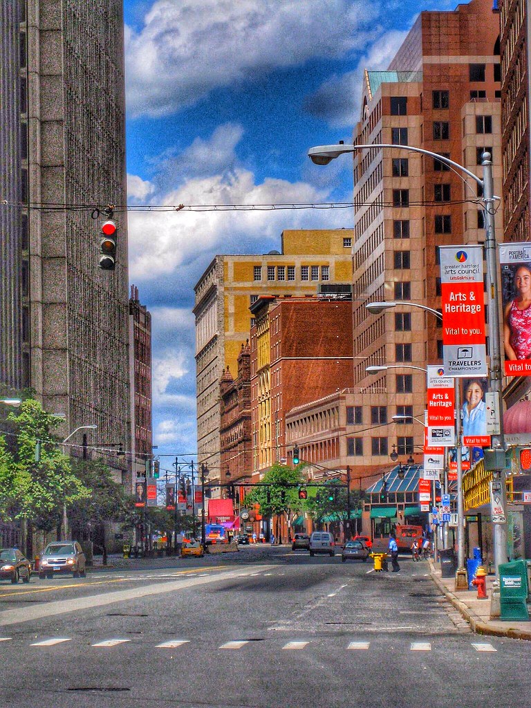 A vibrant city street lined with diverse buildings, cars, and promotional banners under a