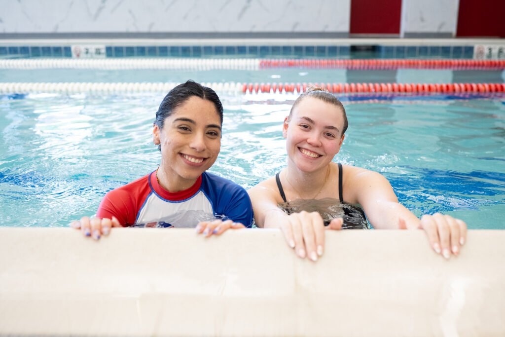 Un instructor de natación sonriente y un estudiante adulto apoyados en el borde de la piscina durante una clase de natación en British Swim School.