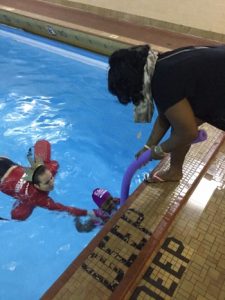 Child swimming in the pool with parent and swim instructor