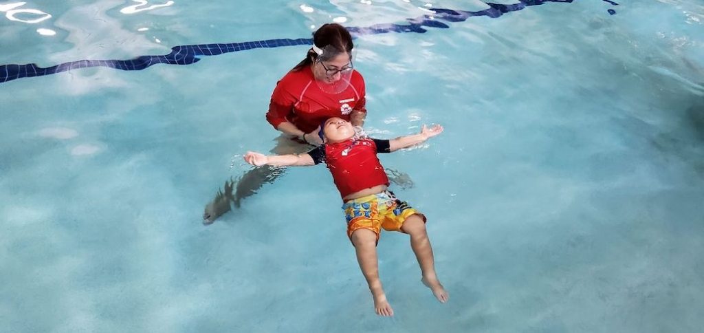 Swim instructor in pool teaching child swim lessons