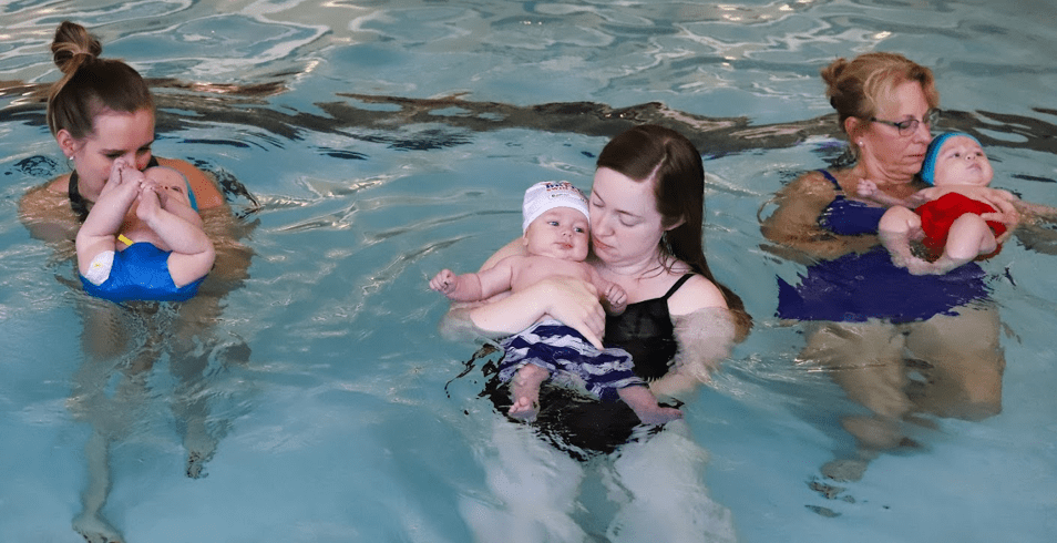 Three moms holding their children in pool during swim class