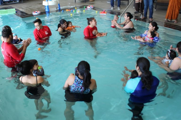 Parents with their children around a swim instructor in the pool