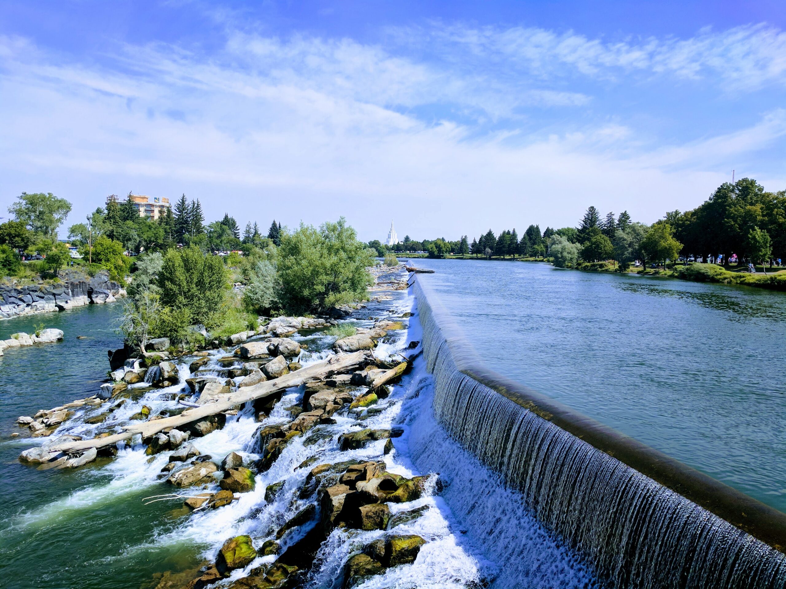A beautiful river cascades over a wide dam and rocky rapids on a sunny day. TITLE