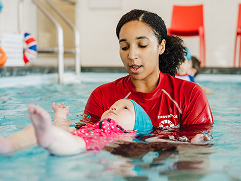 A female swim instructor supports a baby floating on its back in a pool during a