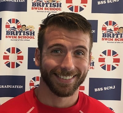 Alex smiling and standing in front of a British Swim School backdrop