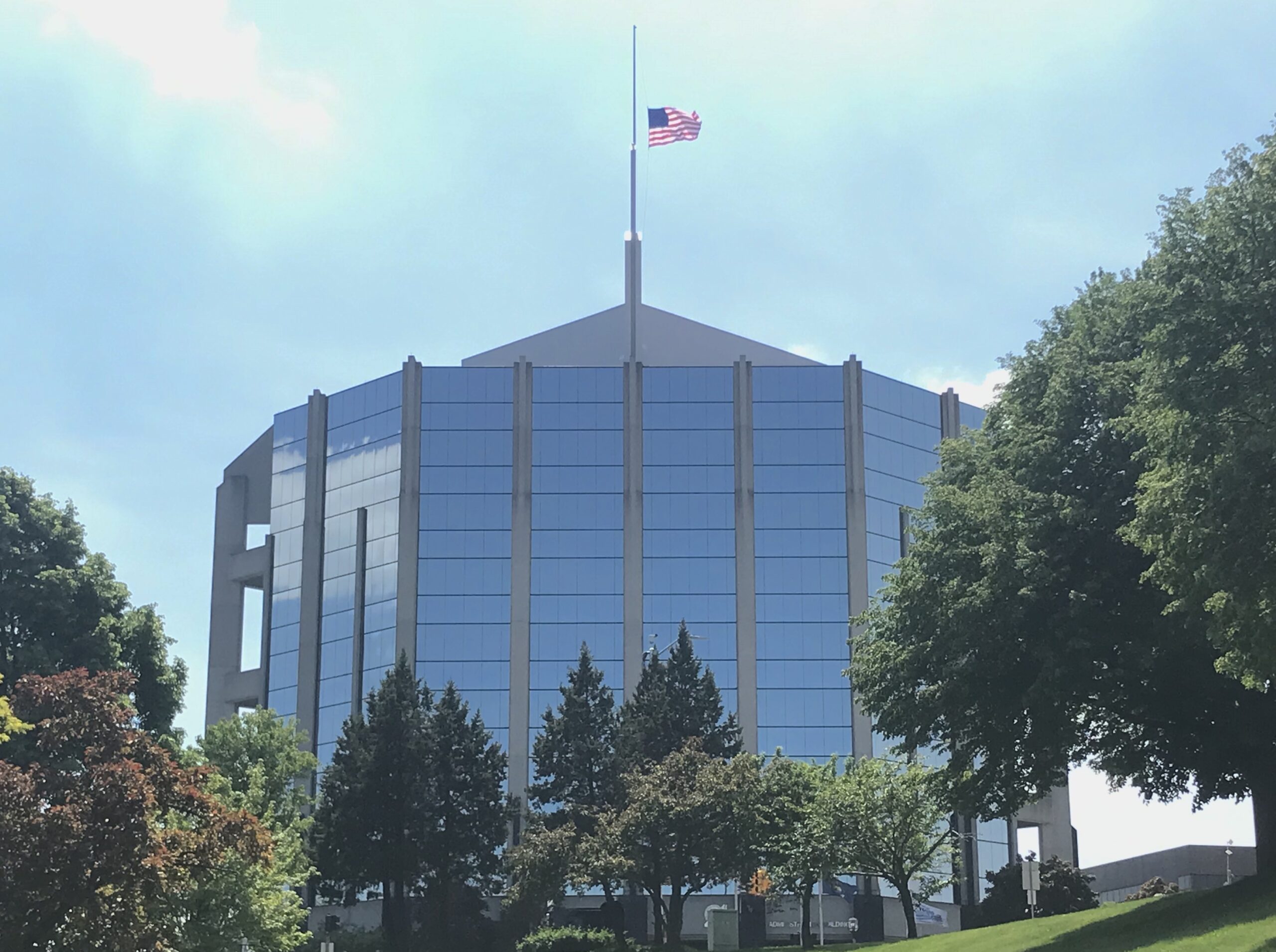 A modern building with blue glass windows flies an American flag at half-staff under a