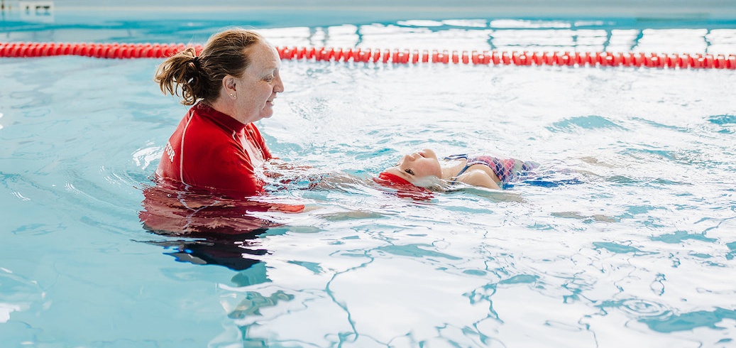 A swimming instructor teaches a young girl to float on her back in a pool.
