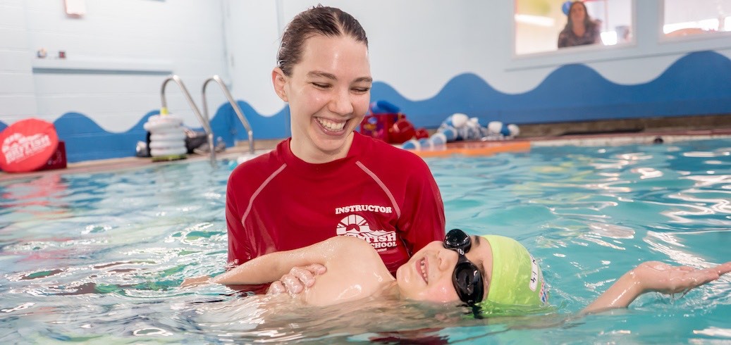A smiling swim instructor teaches a happy child to float on their back in a pool