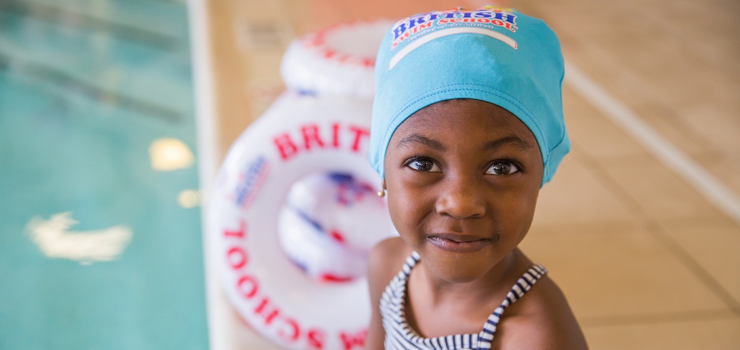 Close-up of a smiling girl wearing a British Swim School swim cap at the