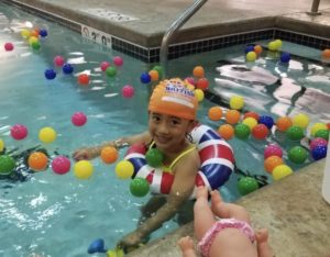 Child floating in the pool with toys