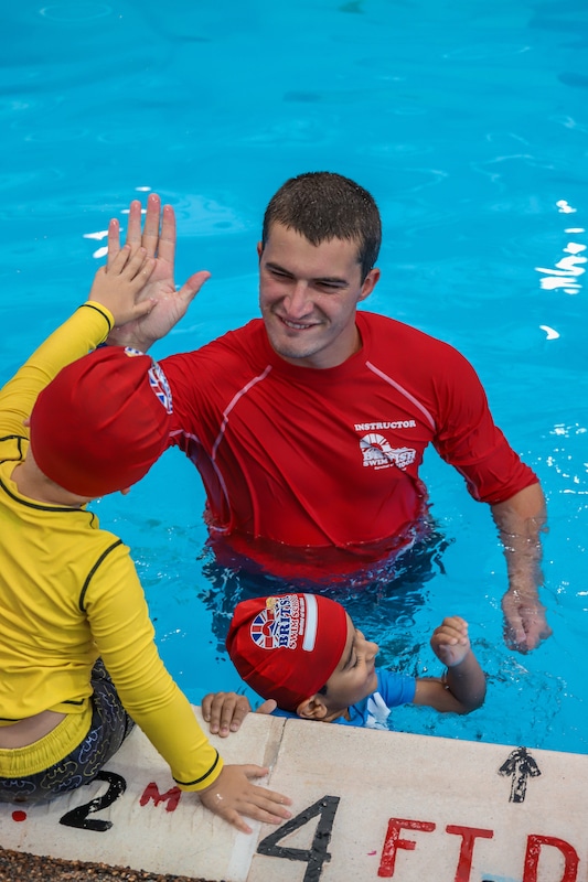 A smiling swim instructor high-fives a child in a pool during a British Swim School