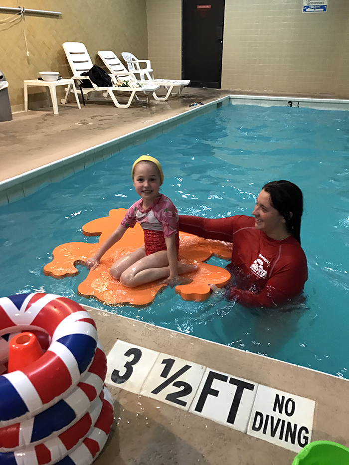 Young woman floating on pool toy with a swim instructor
