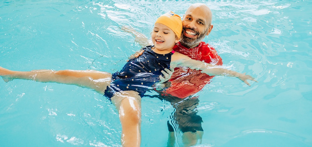 Smiling man and girl enjoy a swimming lesson in a bright blue pool. TITLE