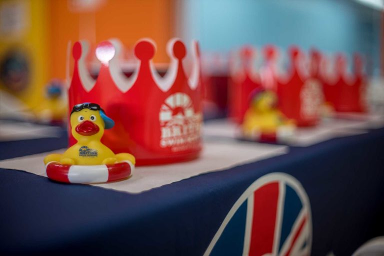 British Swim School branded rubber duck and crown sitting on table top