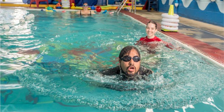 Man swimming in pool with swim instructor