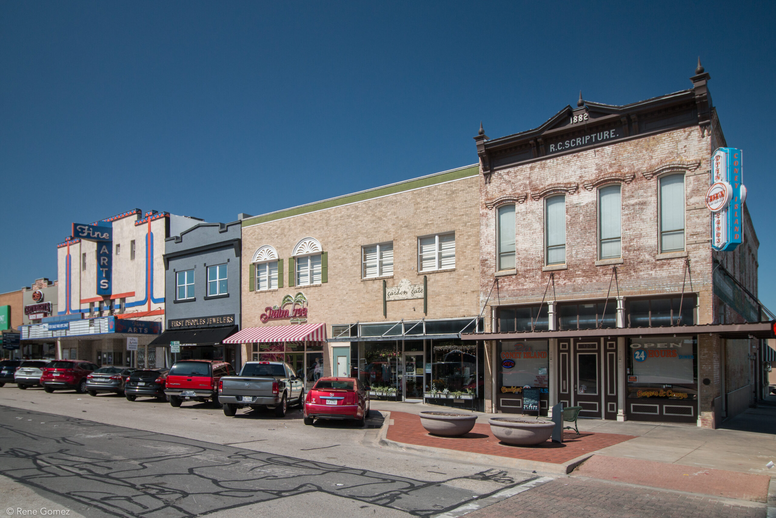 A sunny street scene features a row of historic downtown buildings with diverse shops and a theater