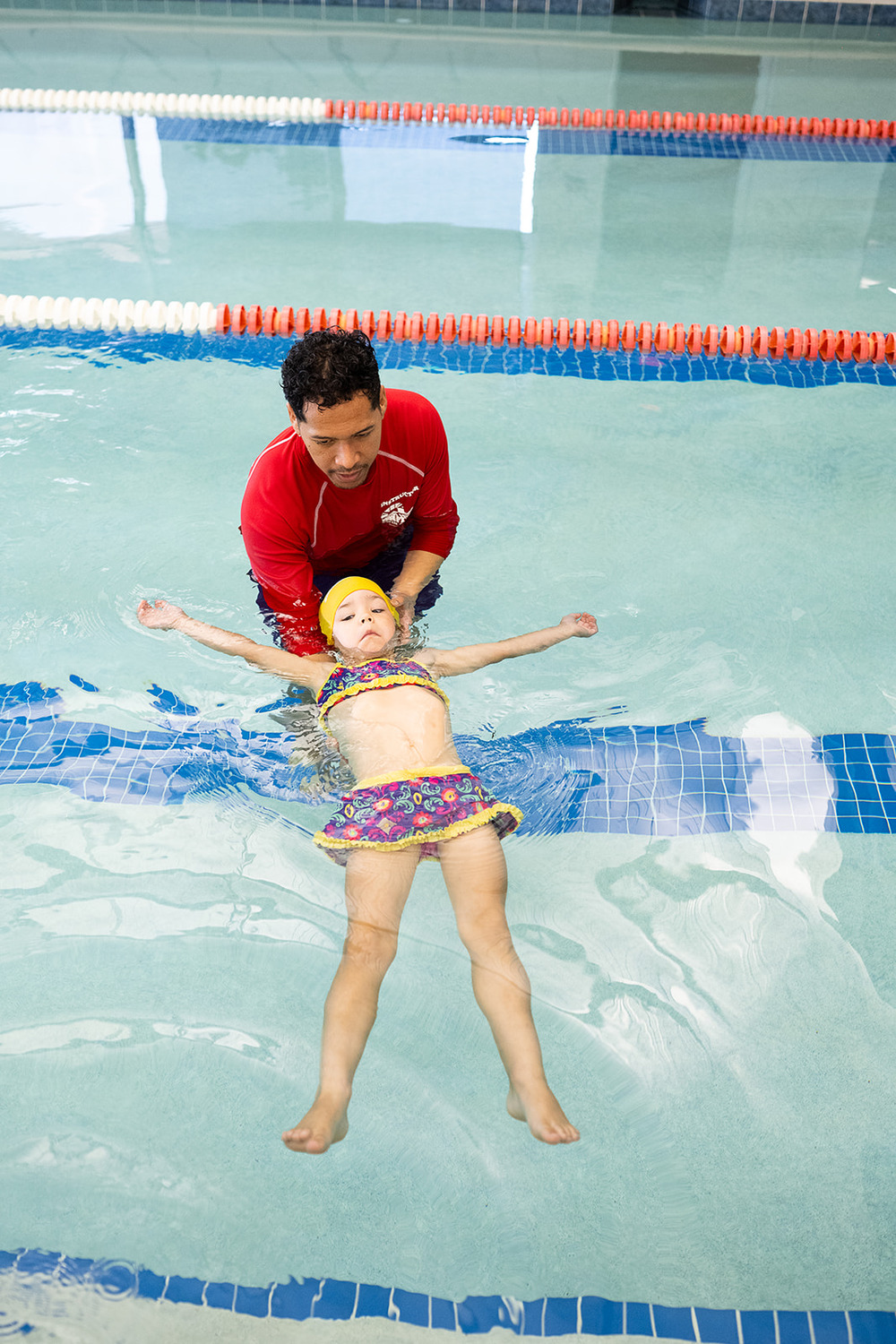 A swim instructor helps a young girl float on her back in a swimming pool.